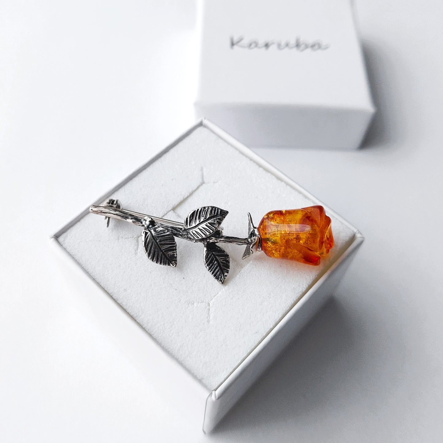 Silver brooch with an orange gemstone on a white box, brand 'Karuba' visible