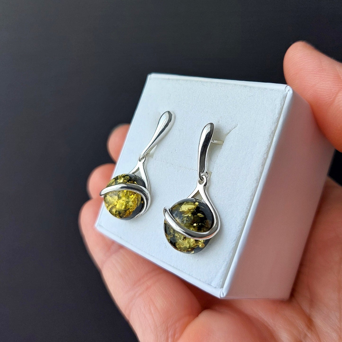 Sterling silver dangle earrings with round green Baltic amber stones on black background