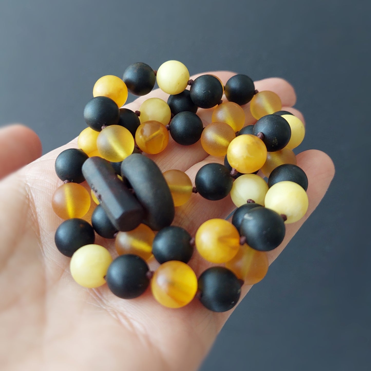Hand holding a bracelet with black and yellow beads against a dark background