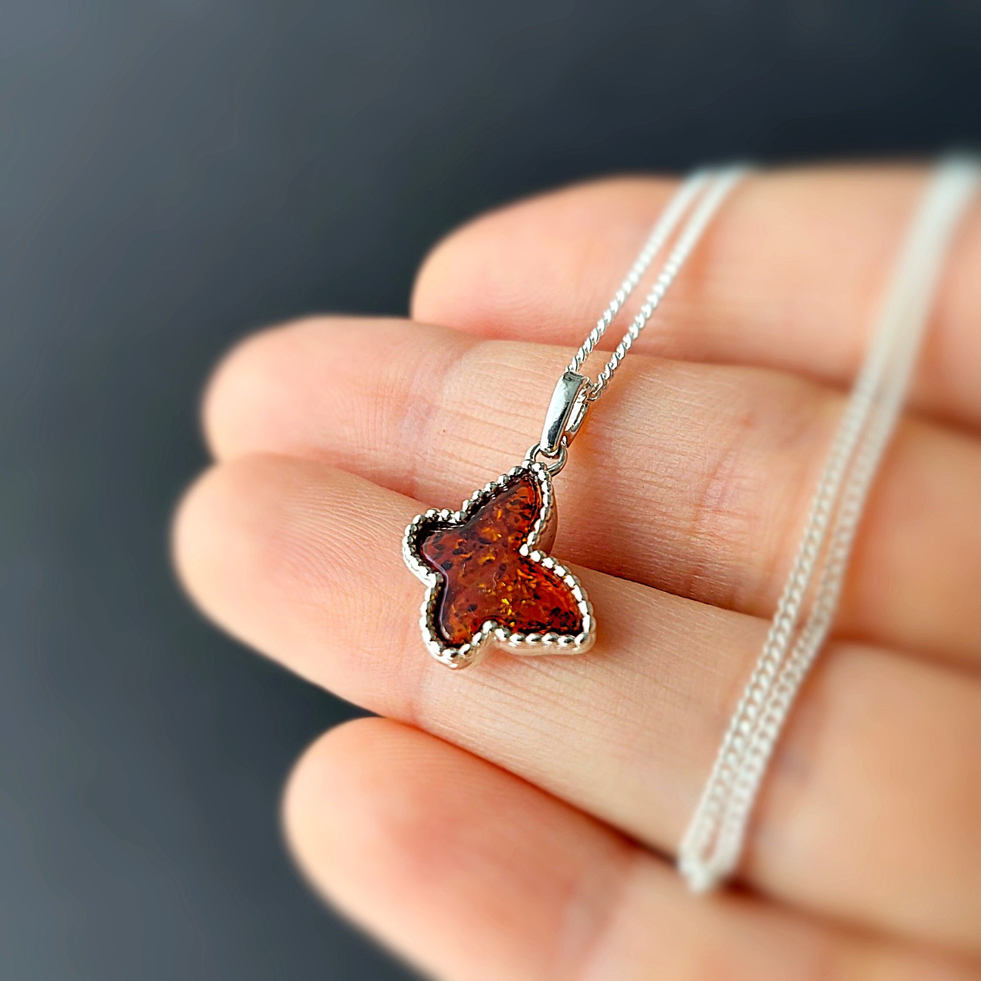 Butterfly-shaped amber pendant on a silver chain held in hand against a dark background