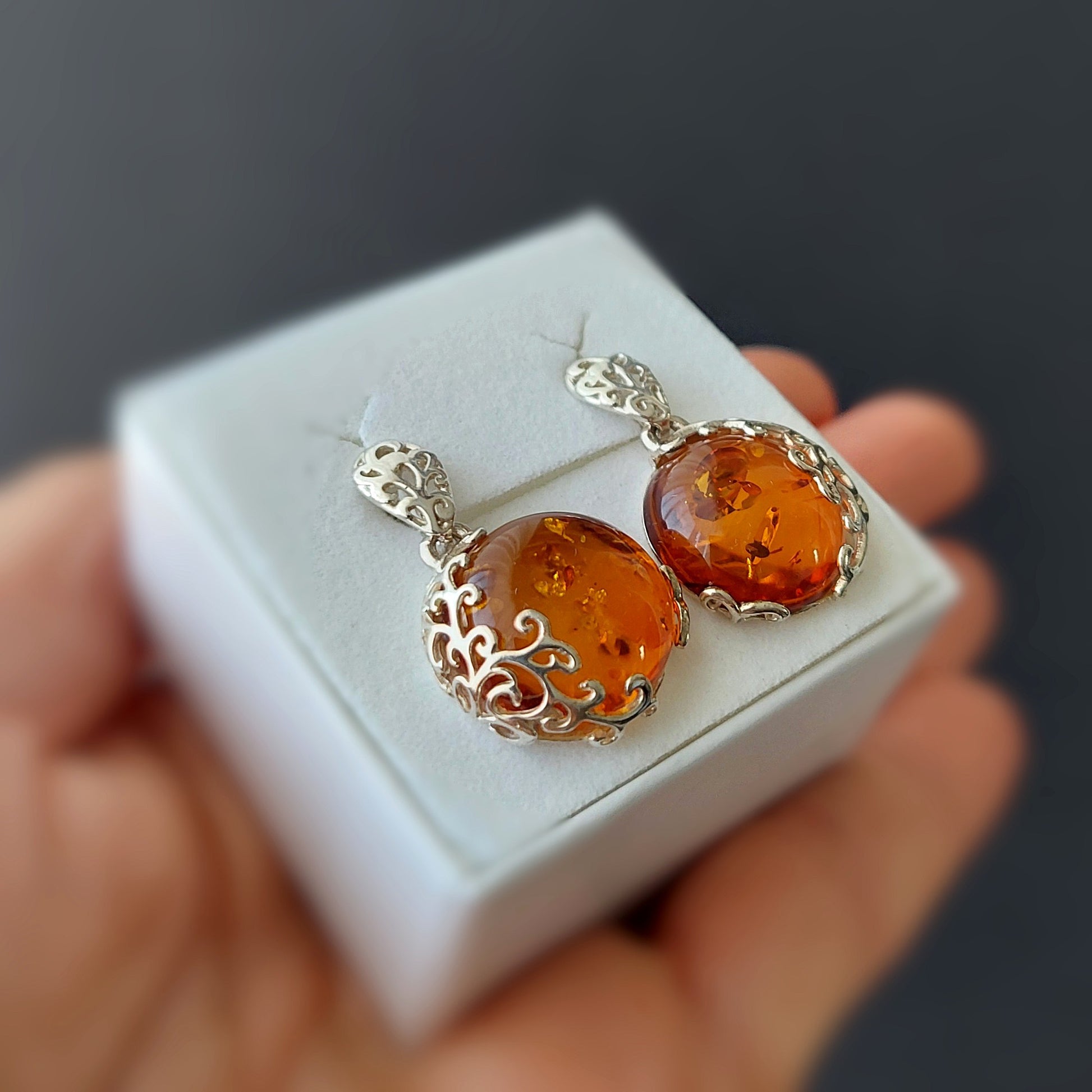 Amber earrings with silver settings on a white box held by a hand against a dark background