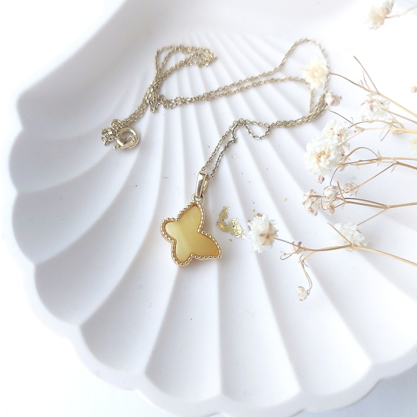 Gold butterfly necklace on a white shell with dried flowers
