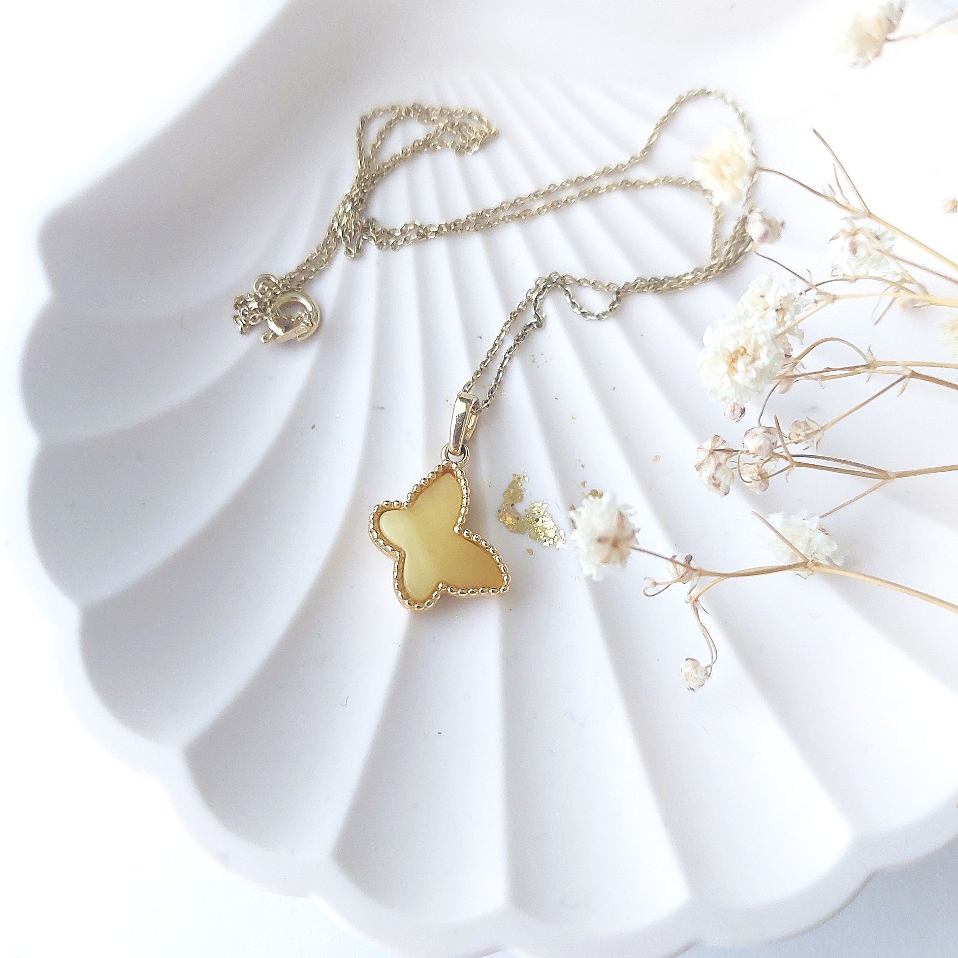 Gold butterfly necklace on a white shell with dried flowers