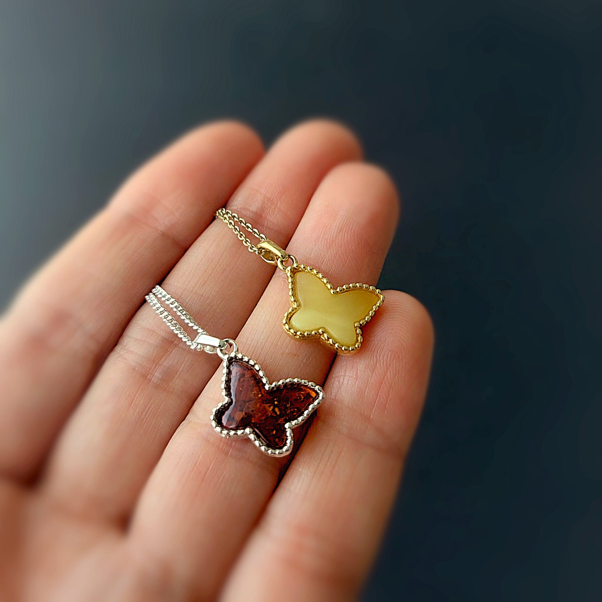 Butterfly-shaped pendants on a chain held in a hand against a dark background