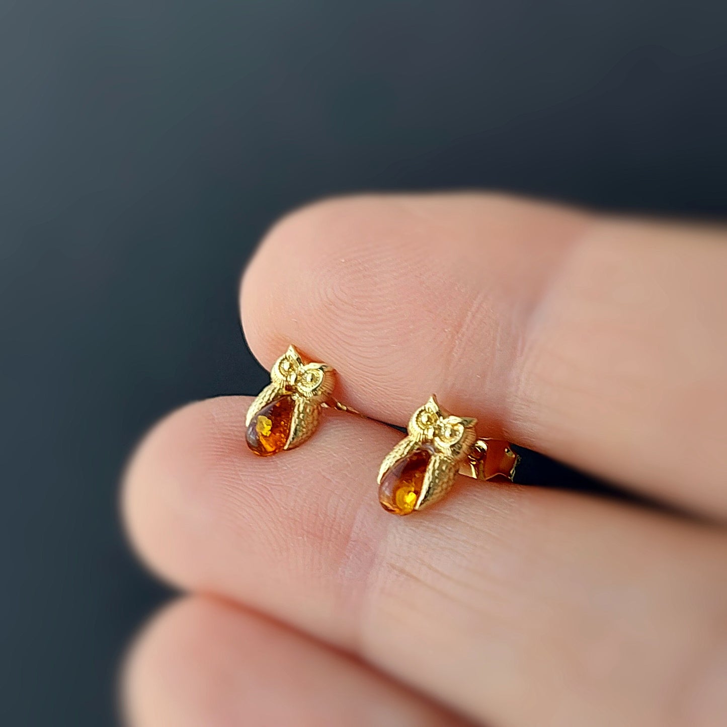 Gold earrings with amber stones held between fingers against a dark background