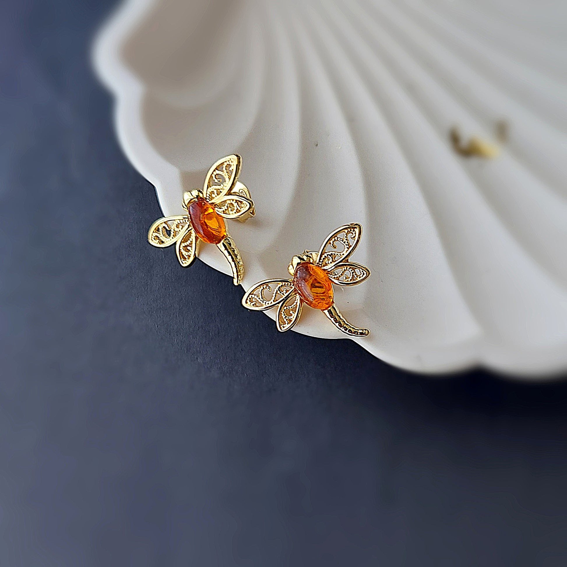 Gold butterfly earrings with orange gemstones on a white shell