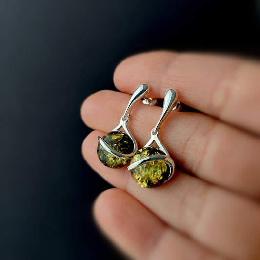 Sterling silver dangle earrings with round green Baltic amber stones on black background