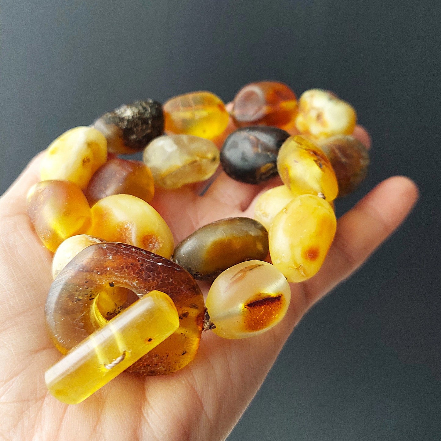 Hand holding a bracelet made of amber beads against a dark background