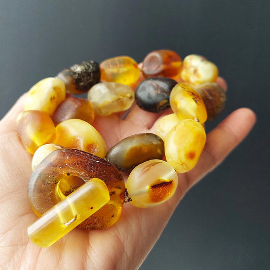 Hand holding a bracelet made of amber beads against a dark background