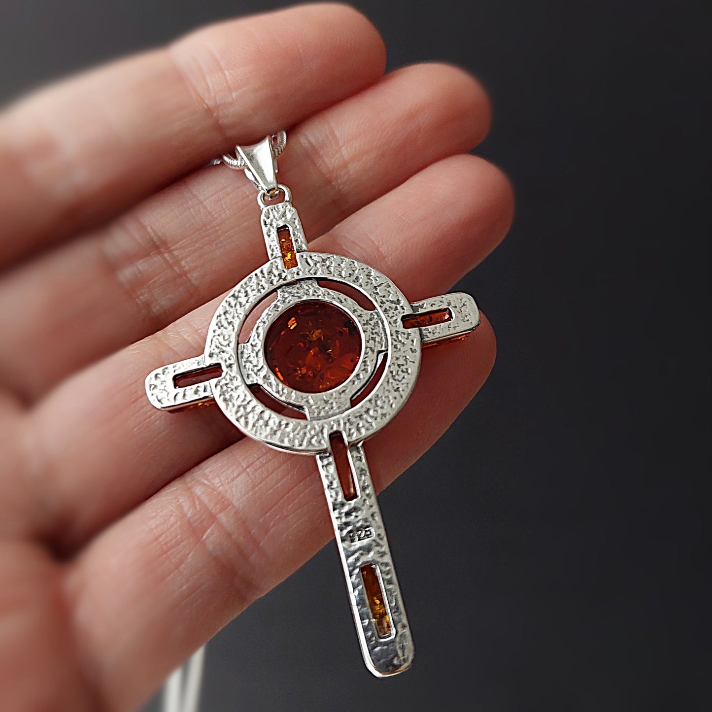 Silver pendant with amber stones held in a hand against a dark background