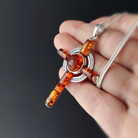 Amber cross pendant on a chain held in a hand against a dark background