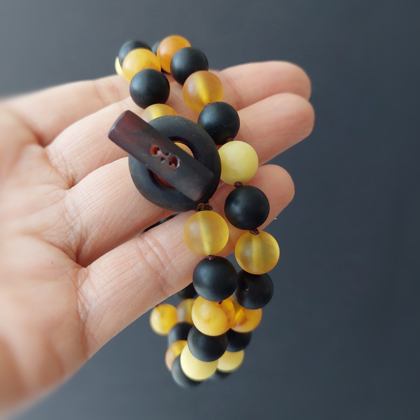 Hand holding a black and yellow beaded bracelet against a dark background