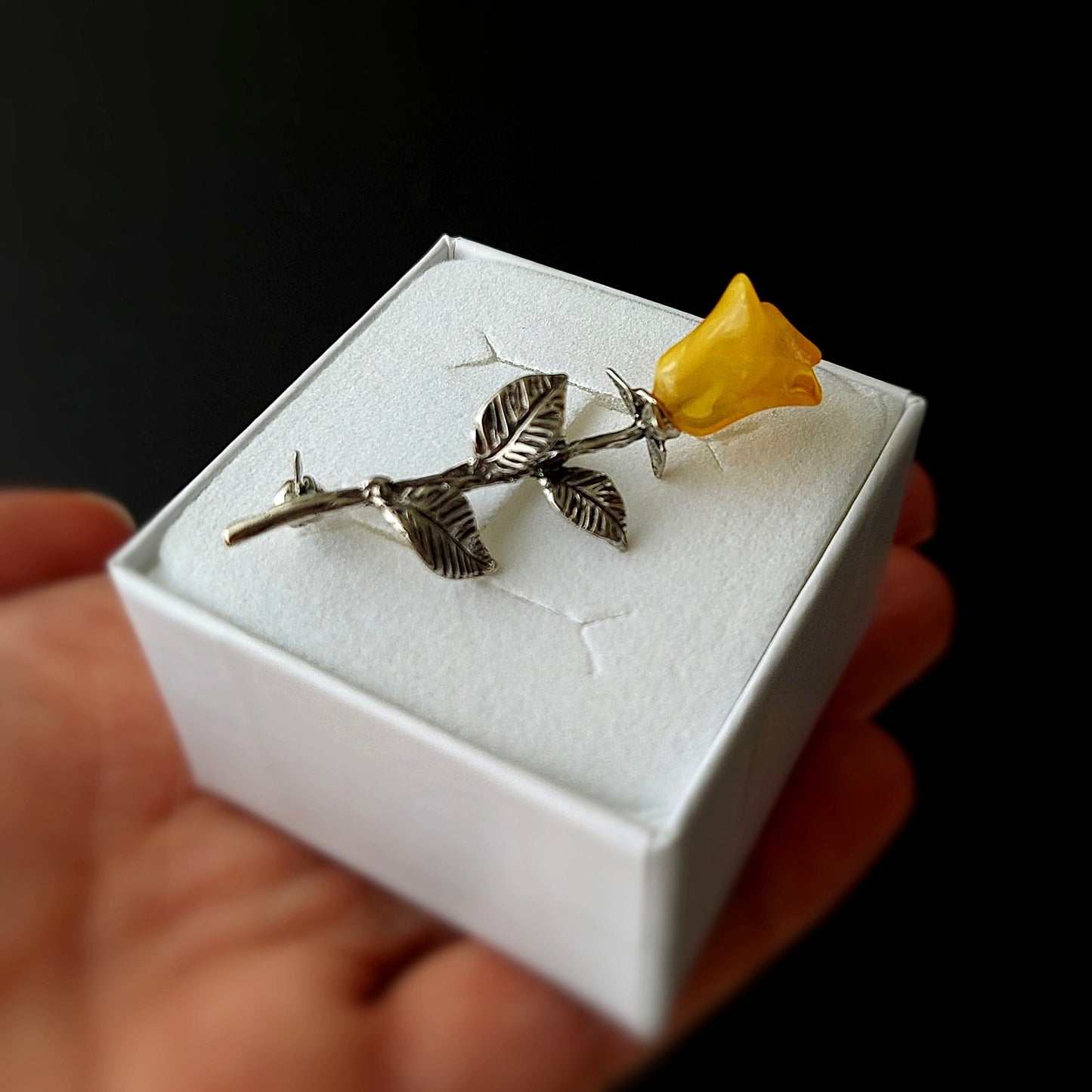 Silver rose with a yellow flower on a white box held by a hand against a black background