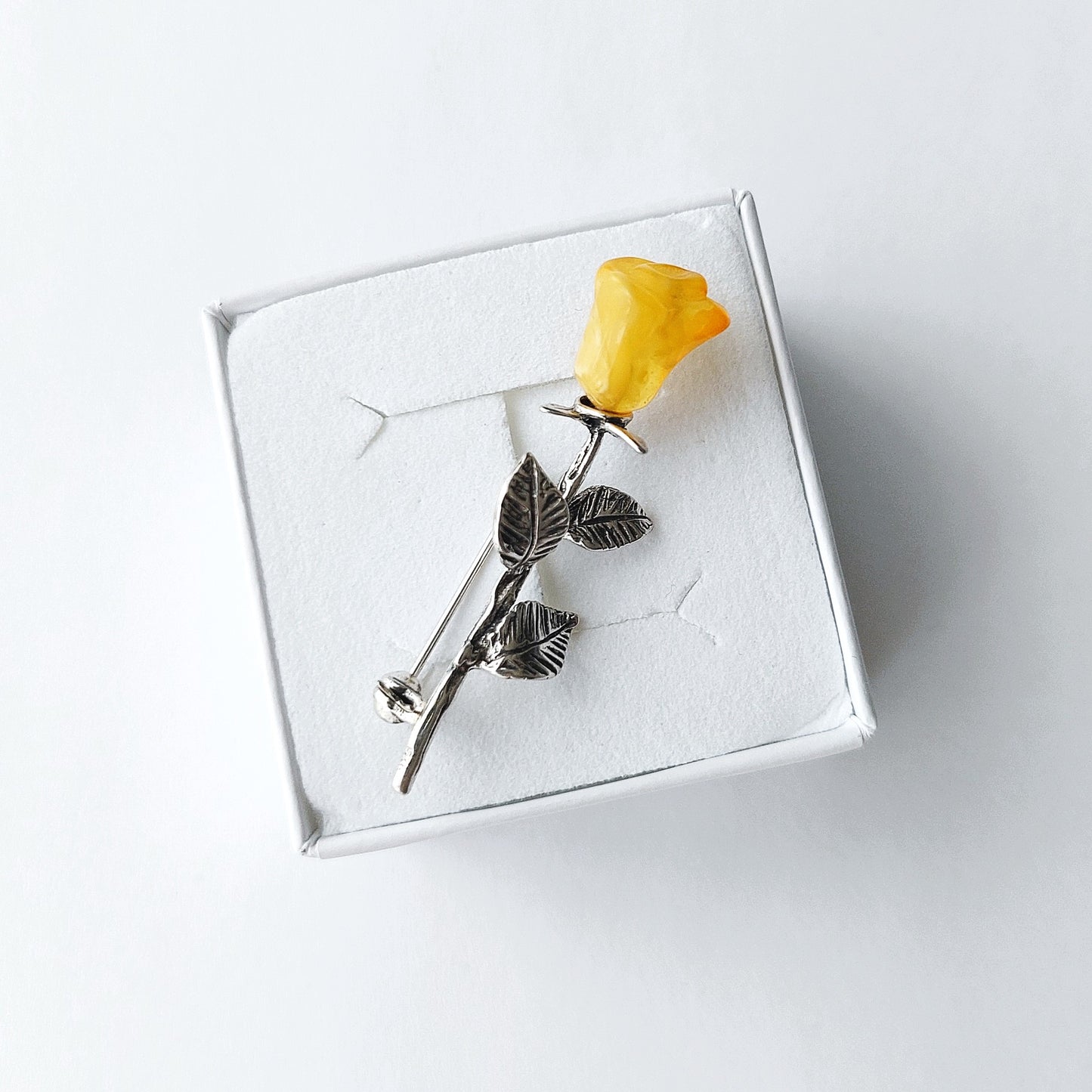 Silver brooch with yellow rose on a white box